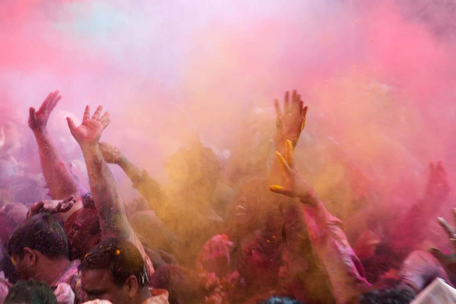 Clouds of coloured powder and raised hands during Holi in Mathura