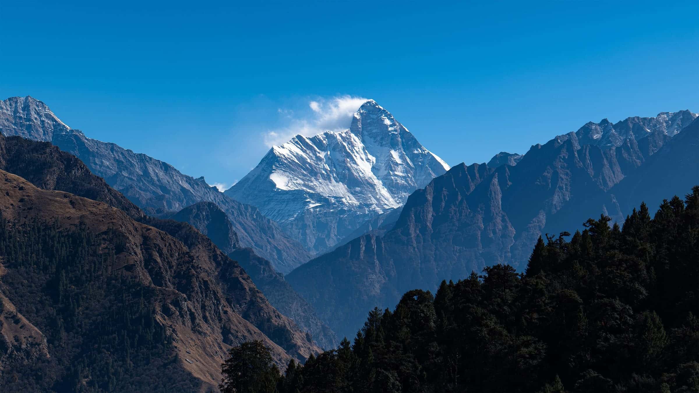 Nanda Devi peak in bright sunlight above forested ridges in Uttarakhand
